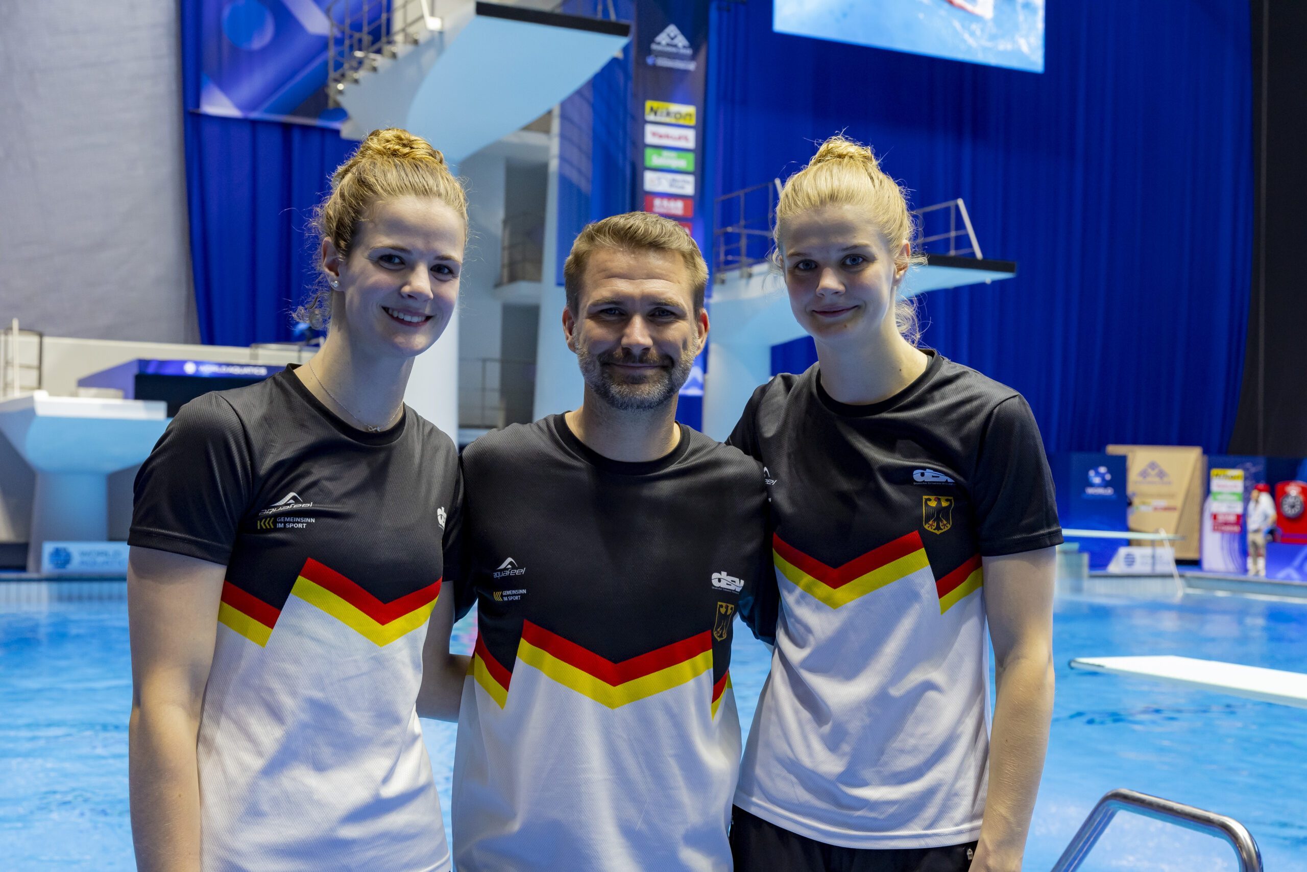 Die Schwestern Elena und Christina Wassen stehen mit ihrem Trainer Christoph Bohm vor der Sprunganlage in Fukuoka (2023)