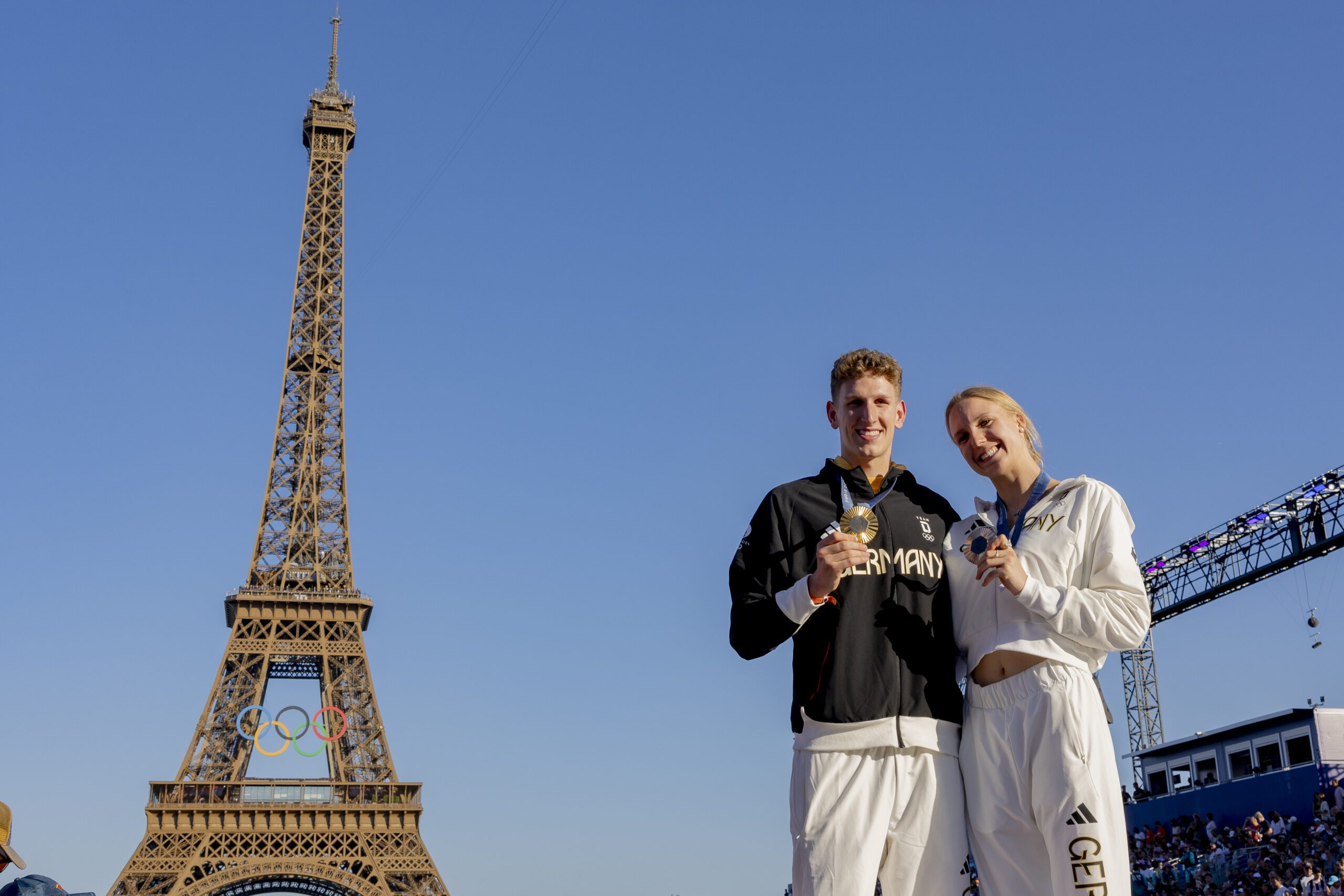 Lukas Märtens und Isabel Gose zeigen ihre Olympiamedaillen vor dem Eiffelturm.