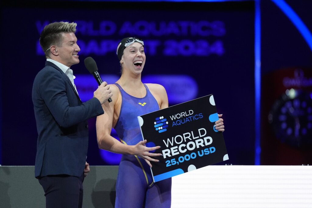 Schwimmer Noe Ponti hält einen Check über 25.000 US-Dollar hoch. Diesen erhielt er für seinen Weltrekord über 50m Schmetterling bei der Kurzbahn-WM in Budapest.