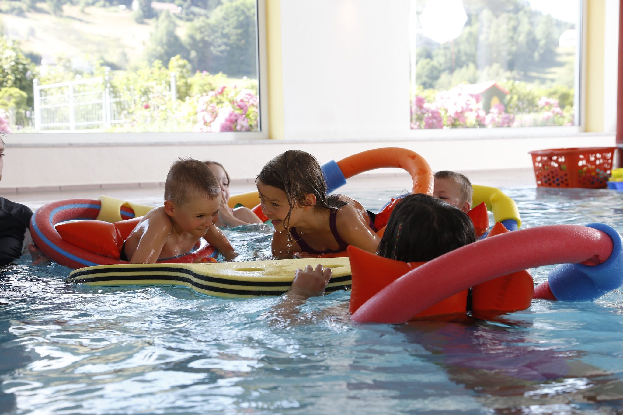 Kinder spielen im Schwimmkurs mit Brettern und Nudeln