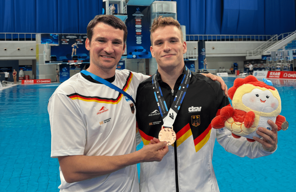 Wasserspringer Moritz Wesemann aus Deutschland steht neben Trainer Norman Becker beim Weltcupfinale 2025 in Peking und zeigt seine Bronzemedaille vom 3m-Brett