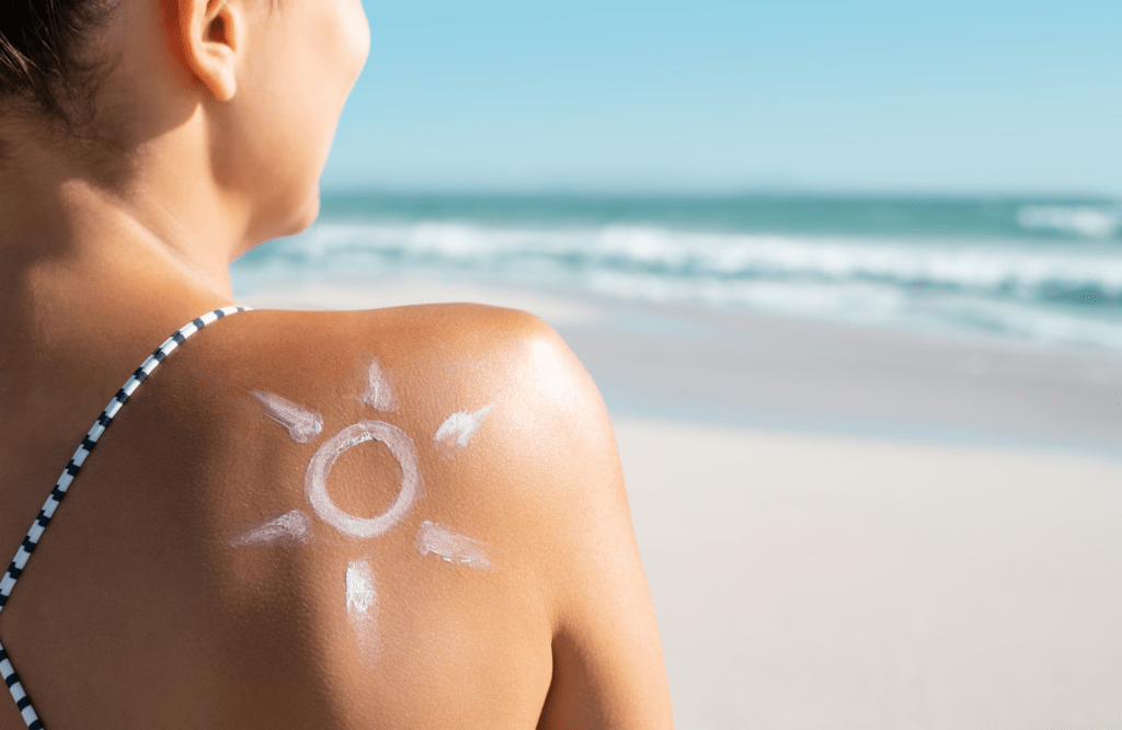 Auf der Schulter einer Frau am Meer ist mit Sonnencreme eine Sonne aufgemalt