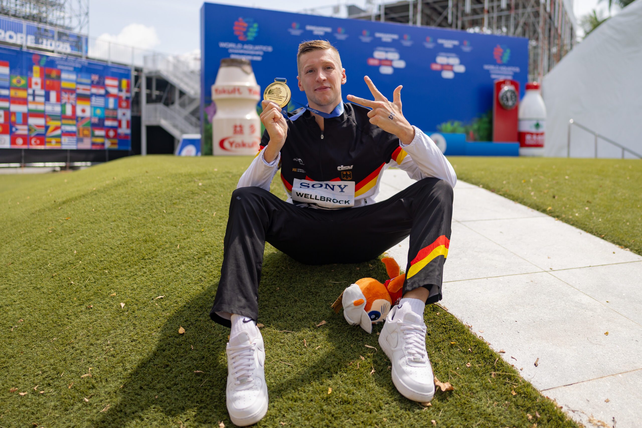 Florian Wellbrock mit seiner dritten Goldmedaille zeigt fröhlich drei Finger