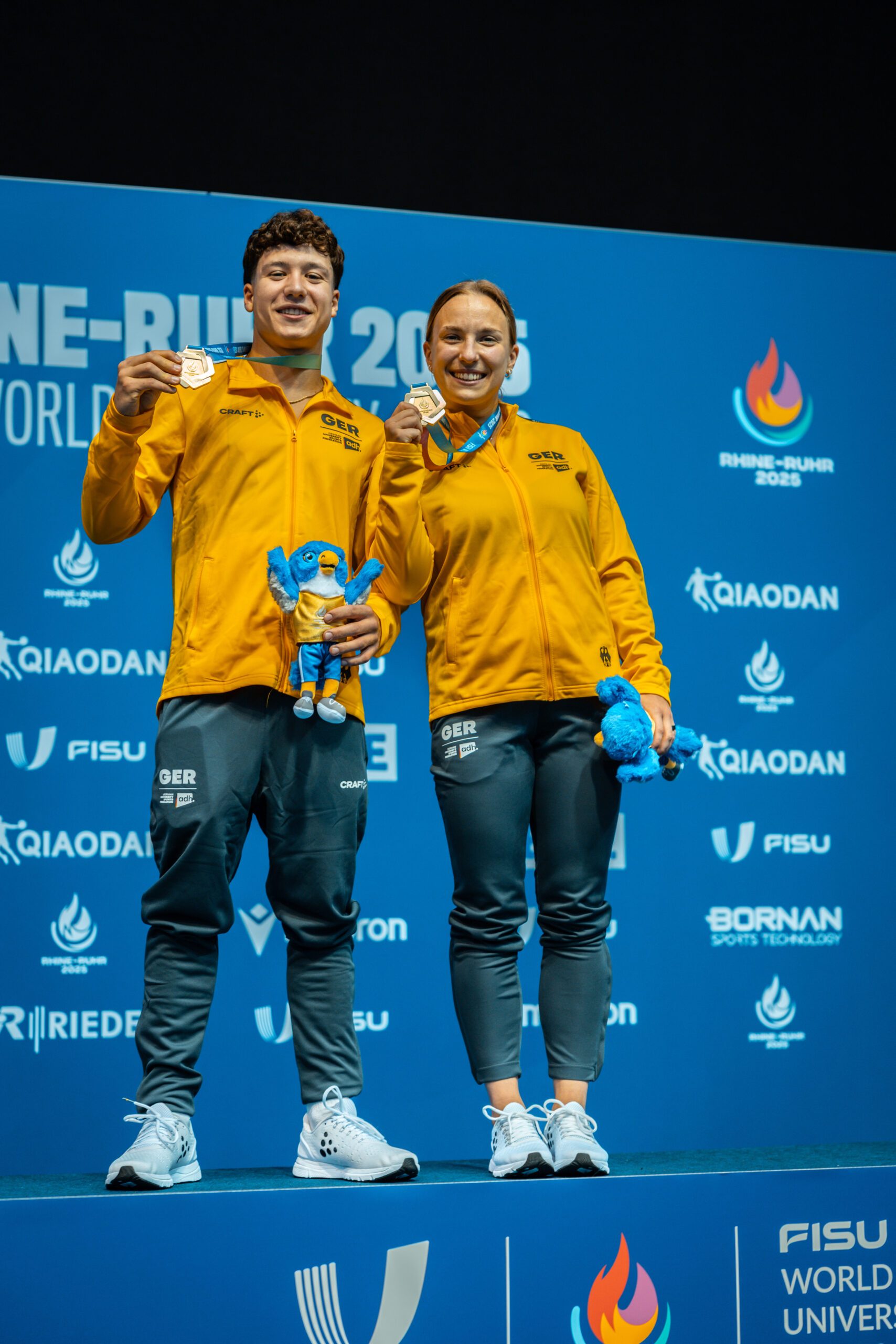 Die Wasserpringer*innen Luis Avila Sanchez und Lena Hentschel aus Deutschland präsentieren ihre Goldmedaillen im Mixed-3m-Synchronspringen bei den World University Games 2025 in Berlin