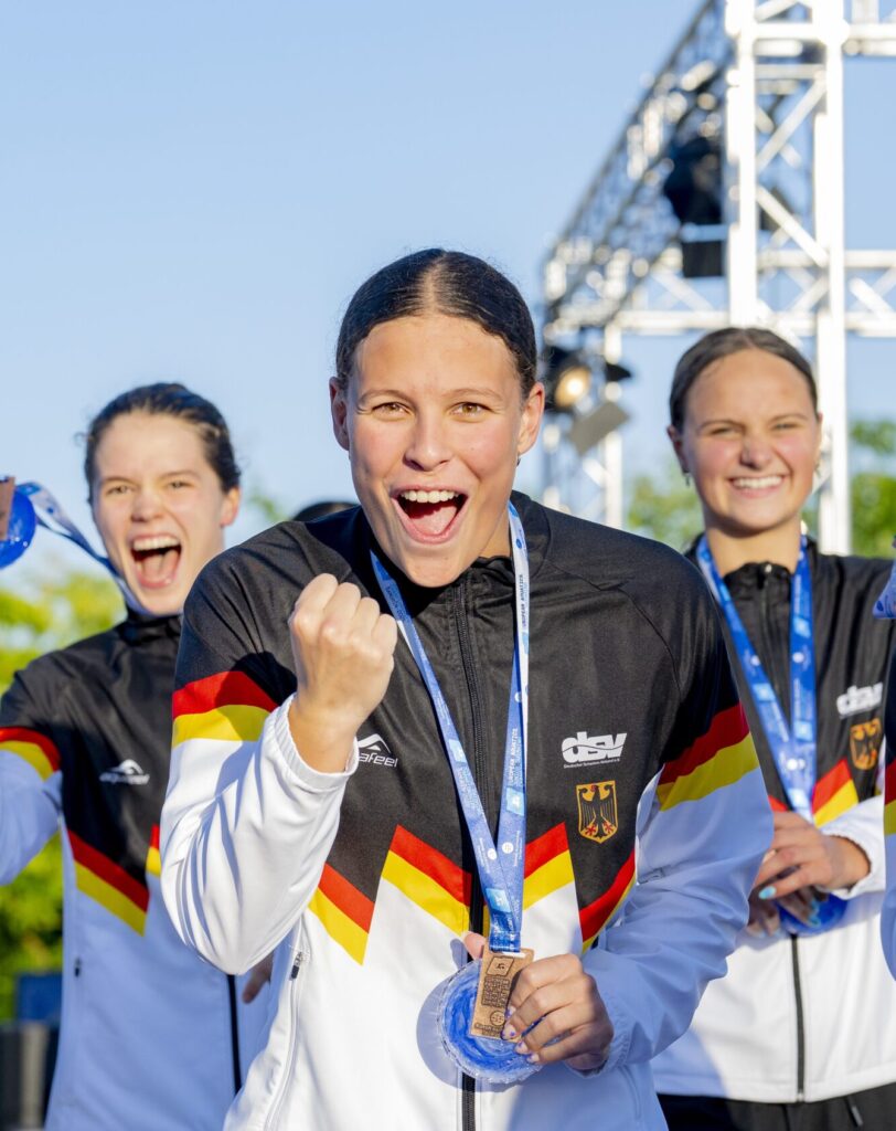 Schwimmerin Linda Roth reckt die Faust in die Luft und jubelt nach ihrer Siegerehrung in die Kamera