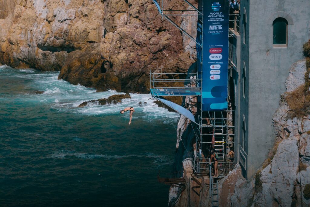 Eine High Diverin springt Weltcup 2025 in Porto Flavio vor den Klippen Sardiniens aus 20m in die Tiefe