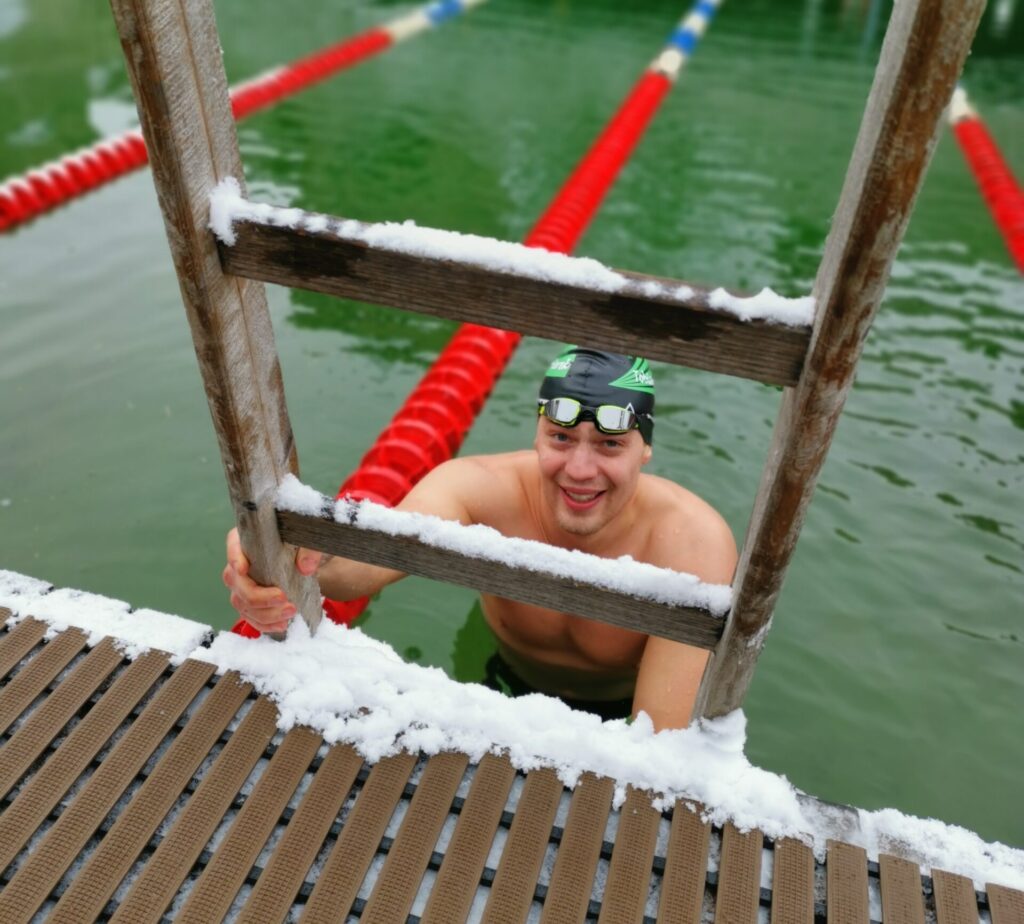 Ein Eisschwimmer steigt an einer Leiter aus dem eiskalten Wasser und blickt in die Kamera