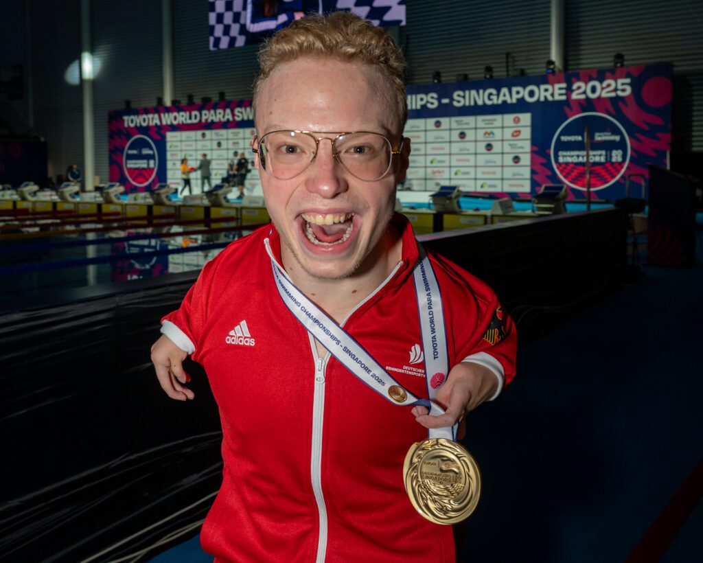 Josia Topf aus Deutschland strahlt nach seinem Sieg bei der Para Schwimm-WM 2025 in Singapur in die Kamera, um den Hals hat er seine Goldmedaille