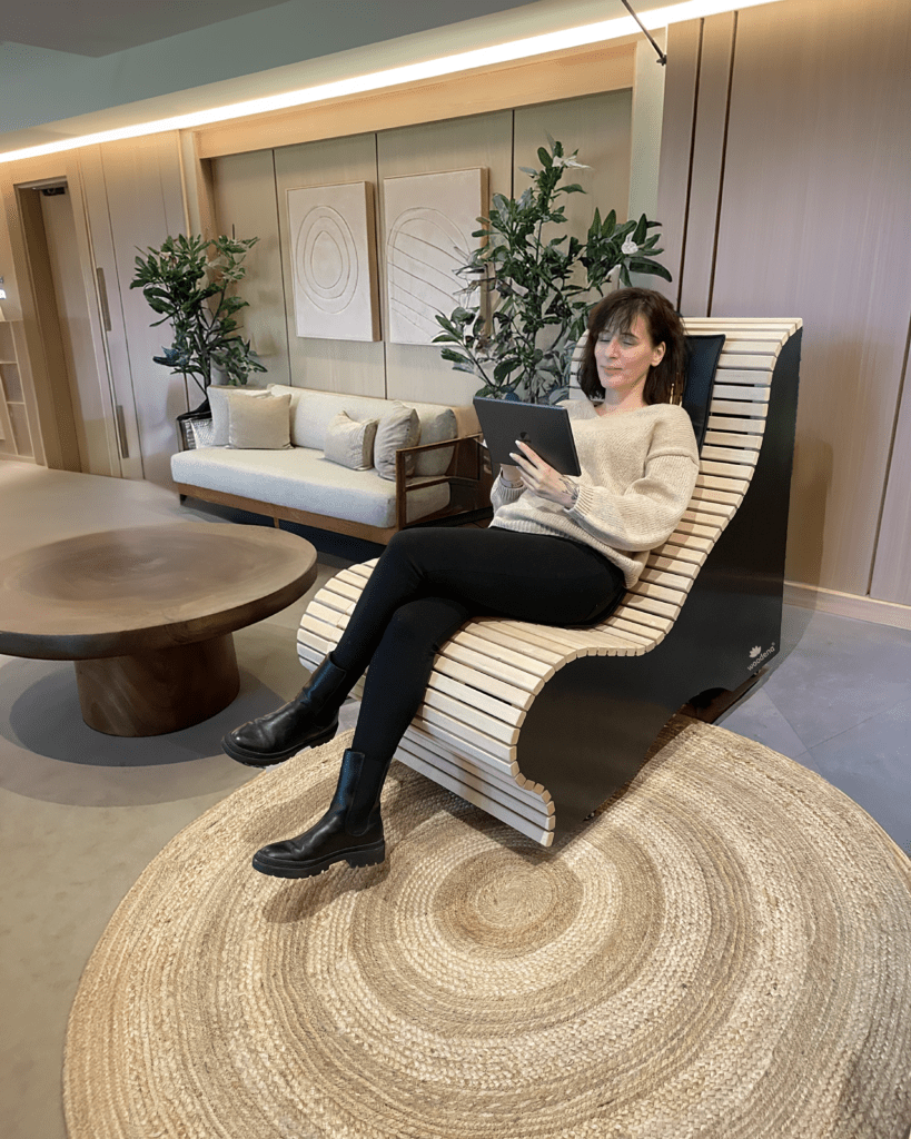 Eine Frau sitzt auf einer wärmenden Infrarotliege und hält dabei ein Tablet in der Hand