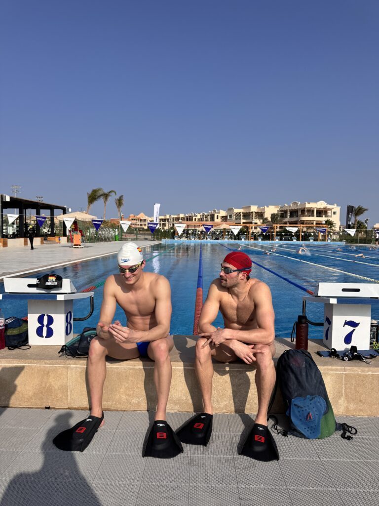 Die deutschen Schwimmer Ole Braunschweig und Luca Nik Armbruster sitzen im Trainingslager in Soma Bay in Ägypten am Beckenrand und tragen dabei Schwimmflossen