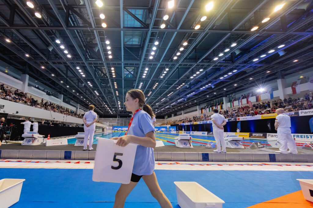 Ein Volunteer trägt bei den Deutschen Meisterschaften 2025 in Berlin eine Kiste mit der Kleidung der Sportler