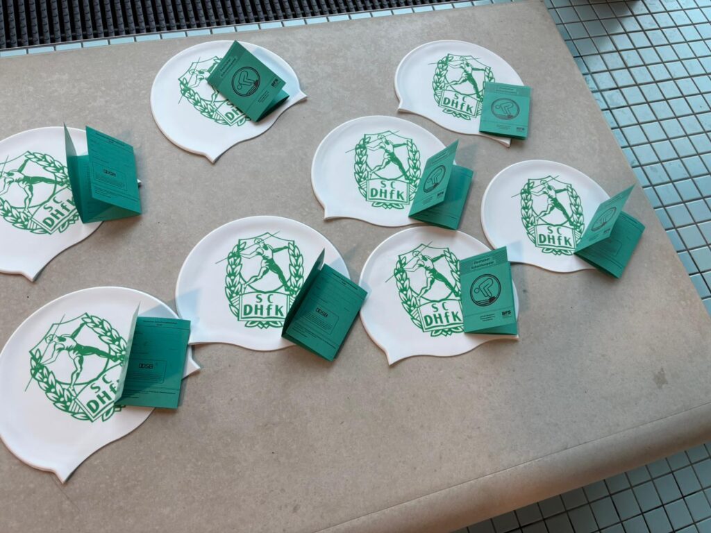 Schwimmabzeichen und Badekappen mit dem Aufdruck des SC DHfK Leipzig liegen am Beckenrand