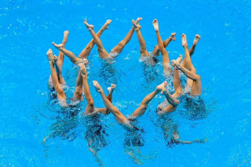 Synchronschwimmerinnen strecken ihre Beine aus dem Wasser im Teamwettbewerb