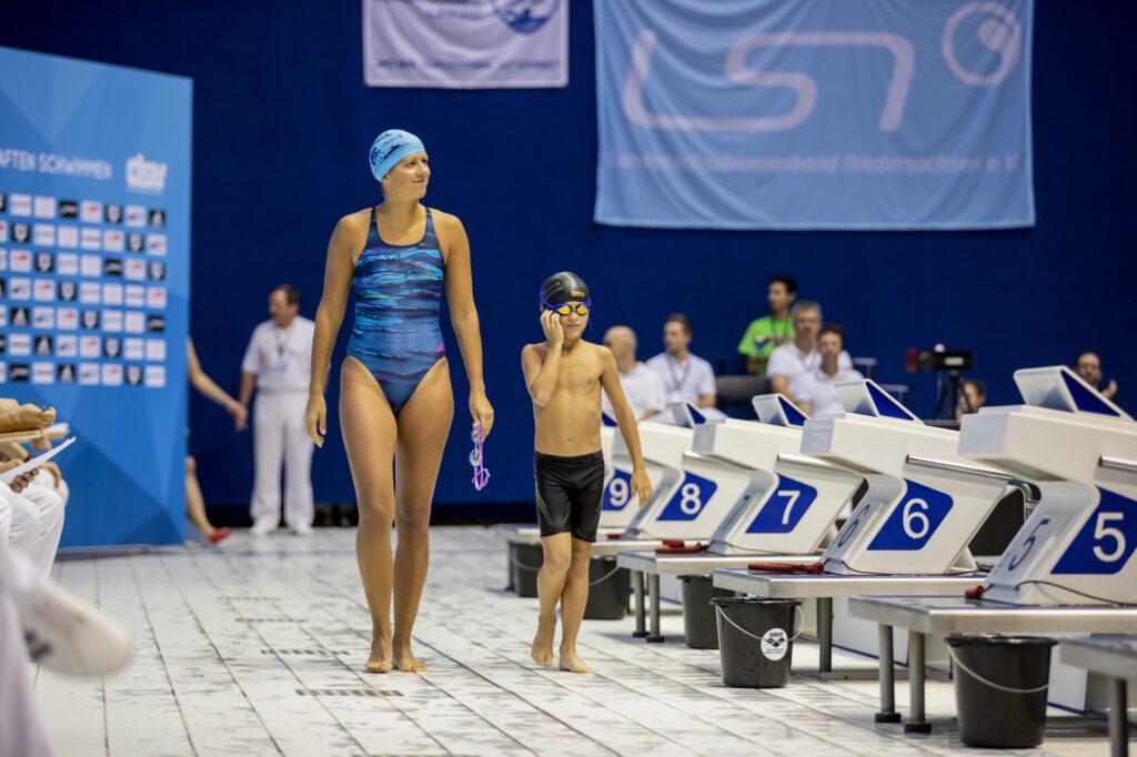 Eine Erwachsene und ein Kind laufen zum Startblock bei einer Familienstaffel im Rahmen der Deutschen Kurzbahnmeisterschaften im Schwimmen 2018 in Berlin