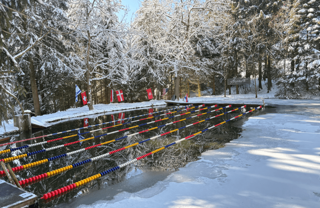 Blick auf die Wettkampffläche bei den Zollhaus Open im Eisschwimmen in Neuhermsdorf im Erzgebirge: Ein See inmitten eines verschneiten Waldes